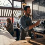 Small café owner updating menu, customers chatting